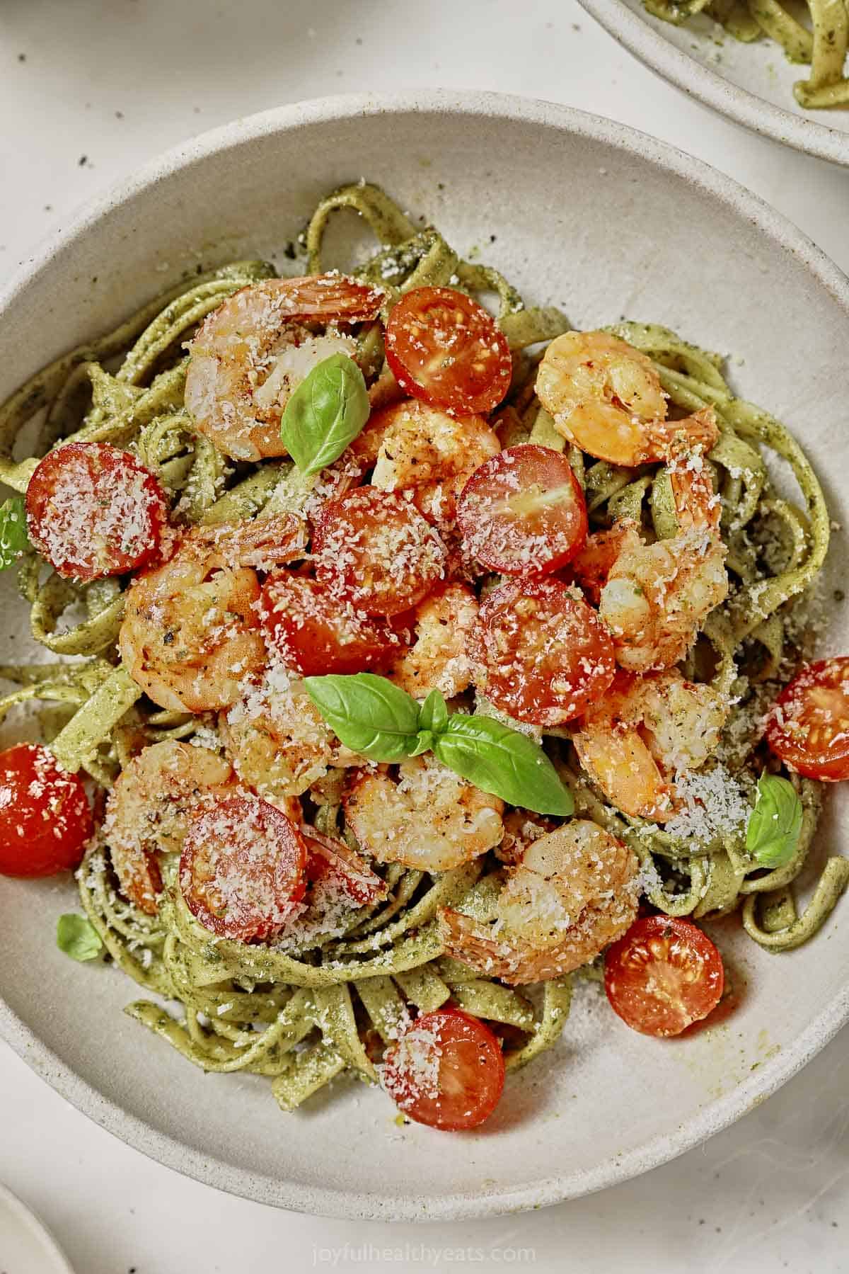 Bowl of shrimp and pesto pasta with juicy tomatoes and parmesan cheese. 