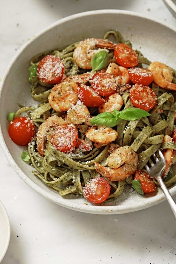 Angled p،to of freshly made pesto pasta with sauteed shrimp, cherry tomatoes, and parmesan cheese.