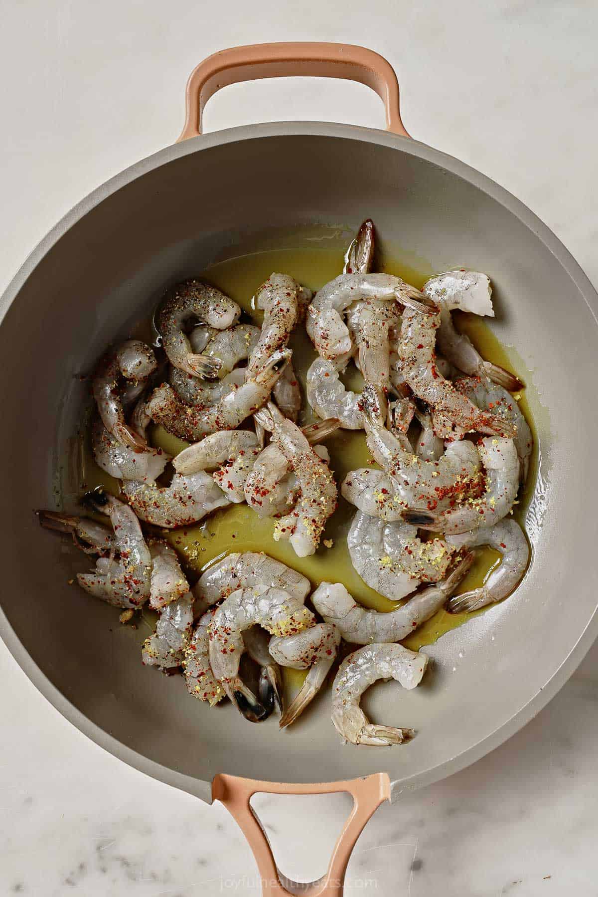 Adding the raw, seasoned shrimp to the pan. 