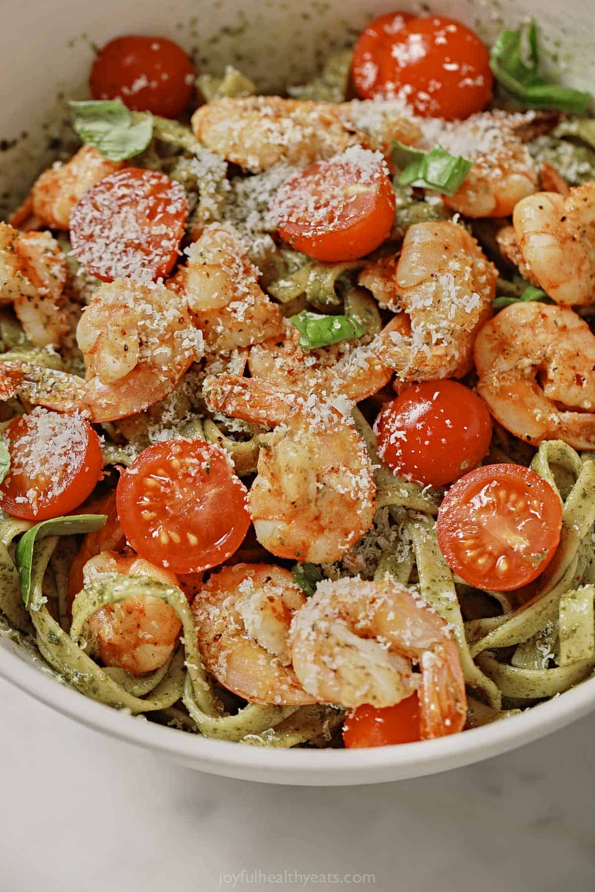 Close-up of pesto pasta with shrimp, tomatoes, and parmesan cheese. 