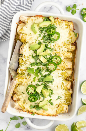 casserole dish with creamy chicken enchiladas verdes with limes and jalapenos as garnishes