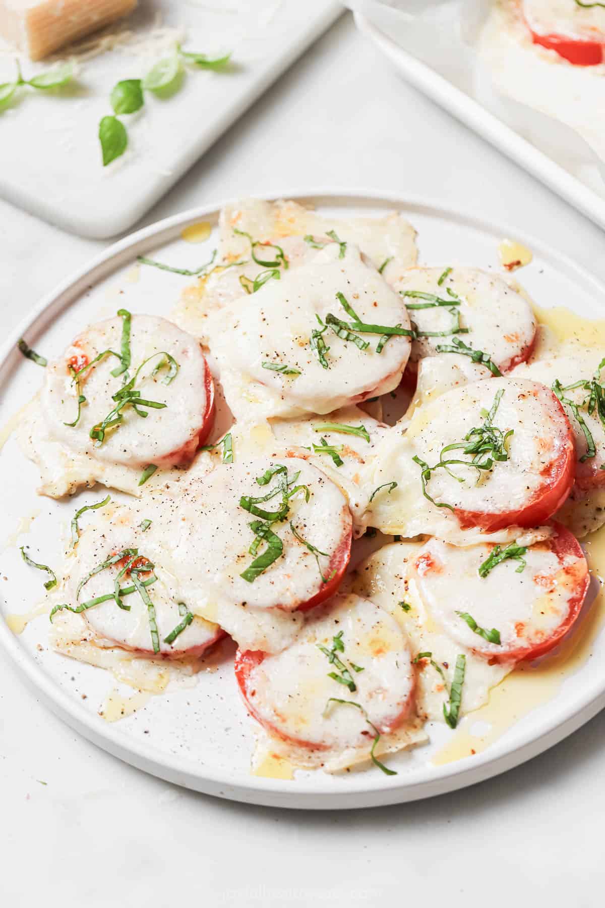 A serving plate of capres-style tomatoes with fresh basil above. 