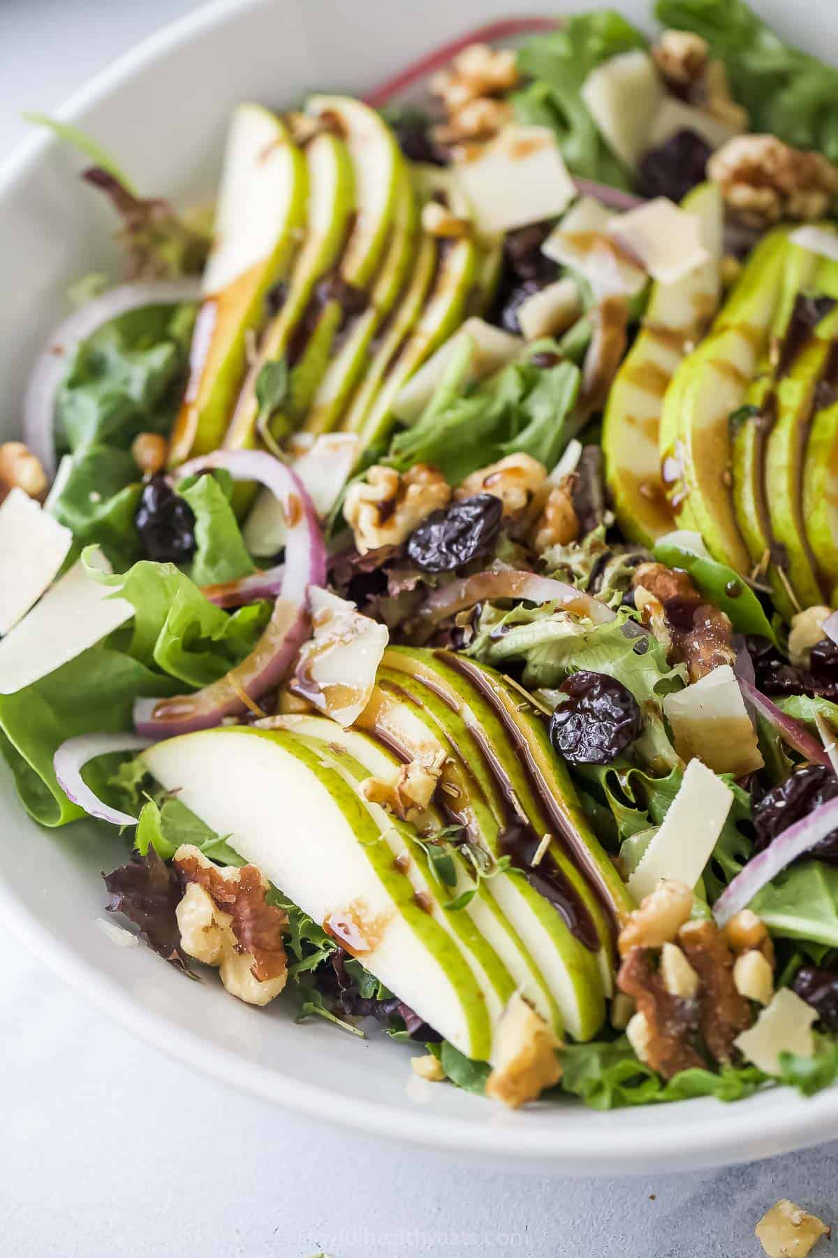 Angled image of fresh walnut salad with pears, cherries, red onion, and parmesan cheese.