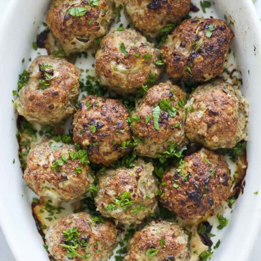 Baked turkey meatballs in the baking dish with parsley on top.