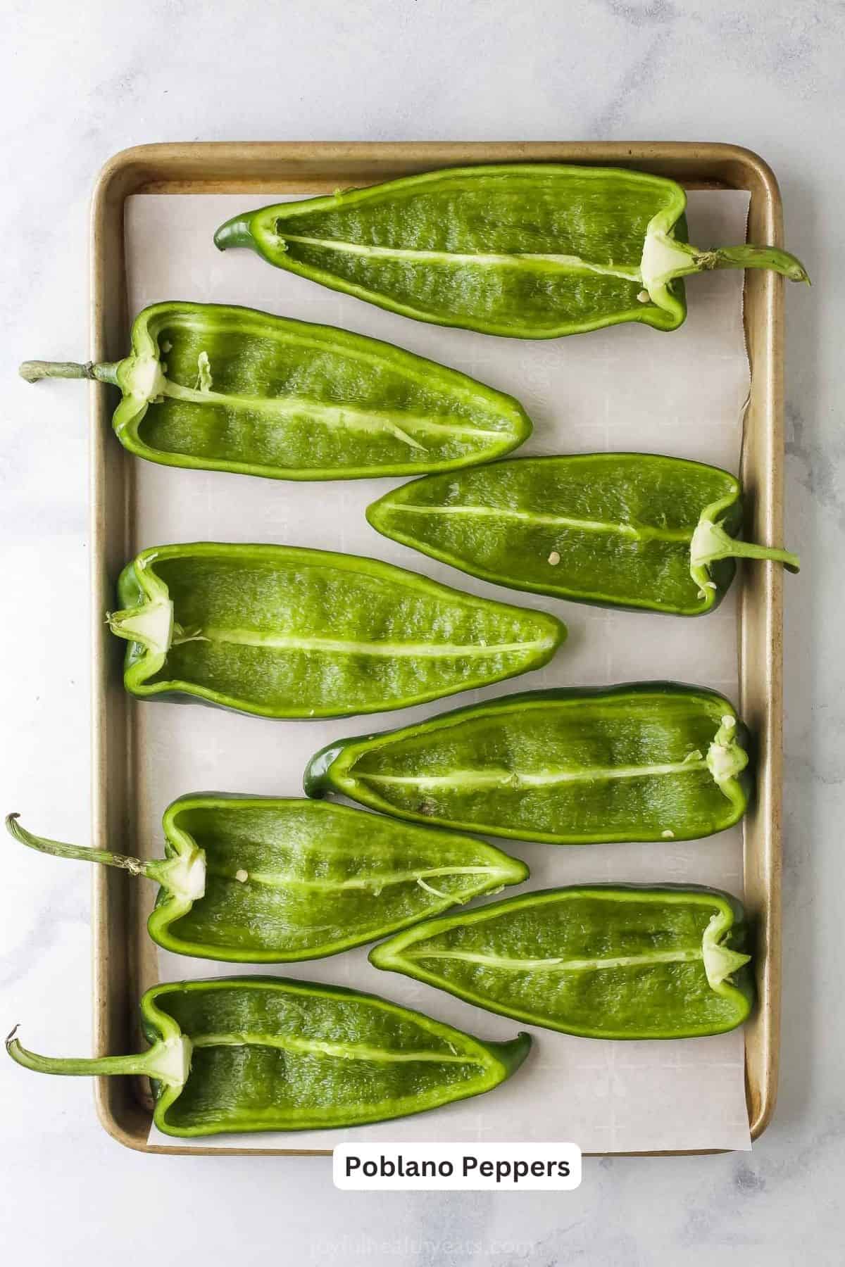 Halved and seeded poblano peppers on a baking sheet ready to be roasted and filled.