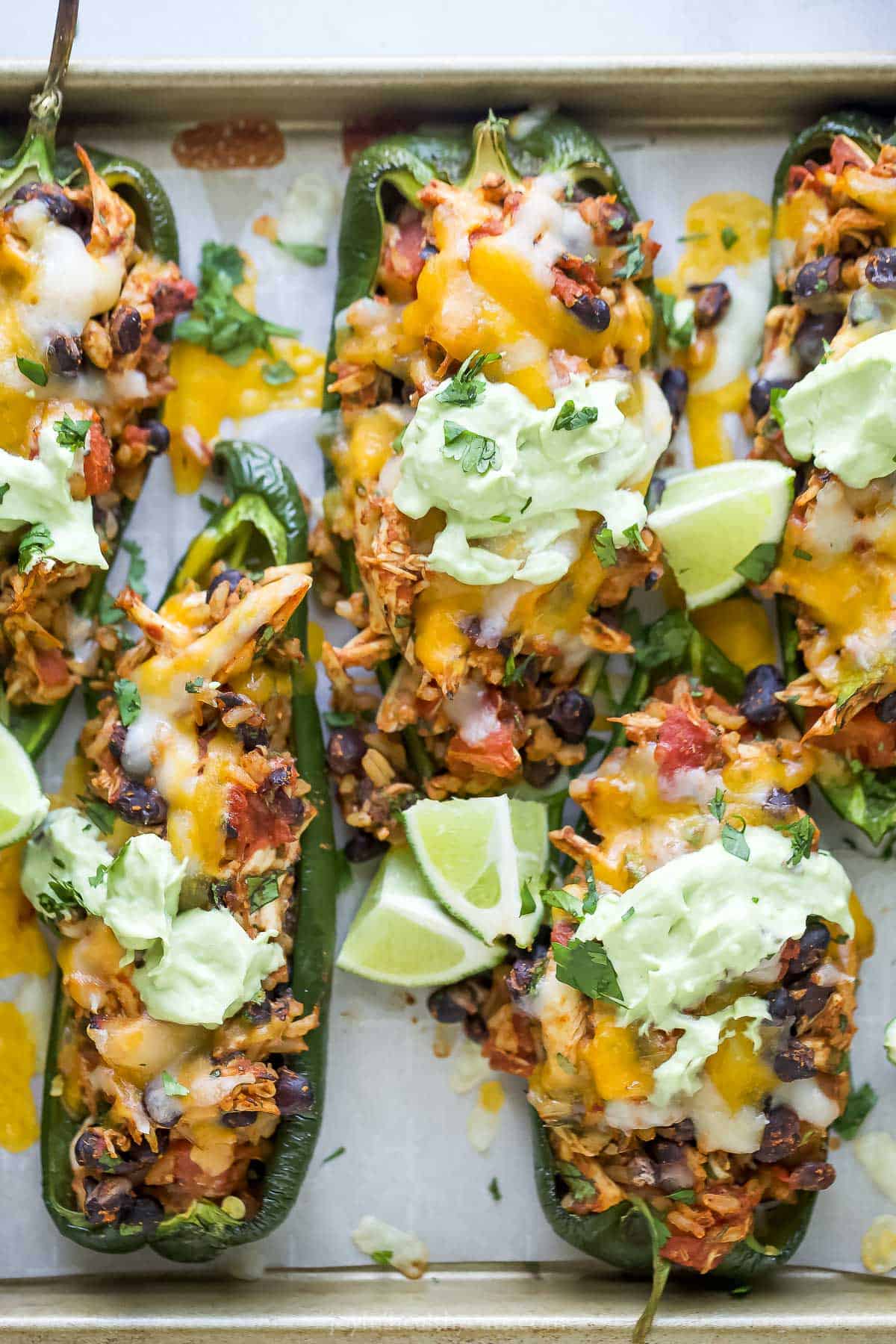 Close-up of baked peppers with melty cheese, fresh cilantro, avocado crema, and lime wedges. 