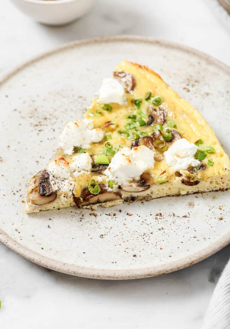 A slice of mushroom frittata with goat cheese and green onions.