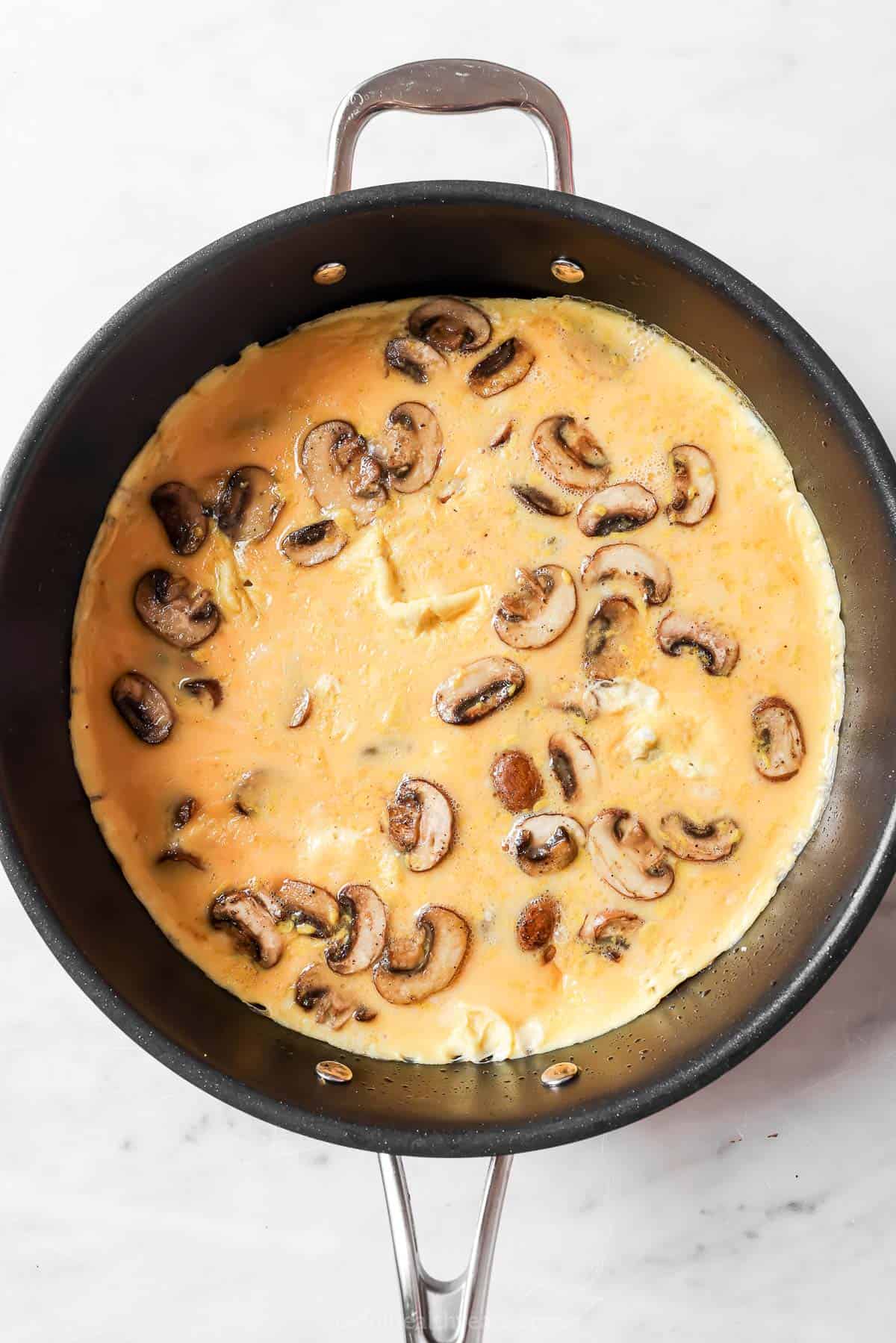 Pouring the egg mixture into the skillet with mushrooms.