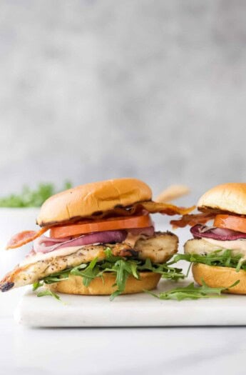 Two sandwiches with chicken, tomatoes, and spring mix salad.