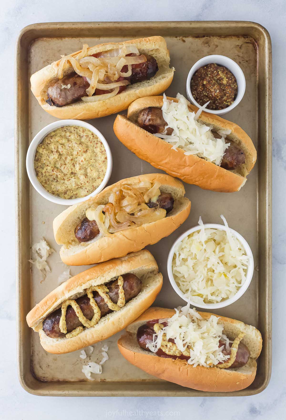 Juicy grilled beer brats on a baking tray with toppings. 