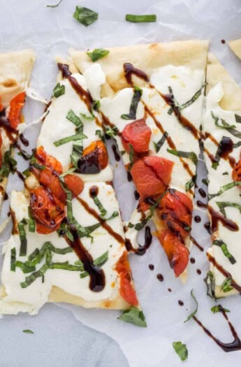 Close-up of pizzas with melty mozzarella, tomatoes, and balsamic reduction.