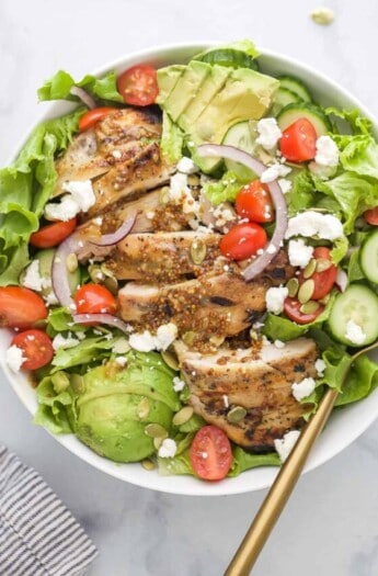 Bowl of chicken salad with avocado, cherry tomatoes, and honey-mustard dressing.