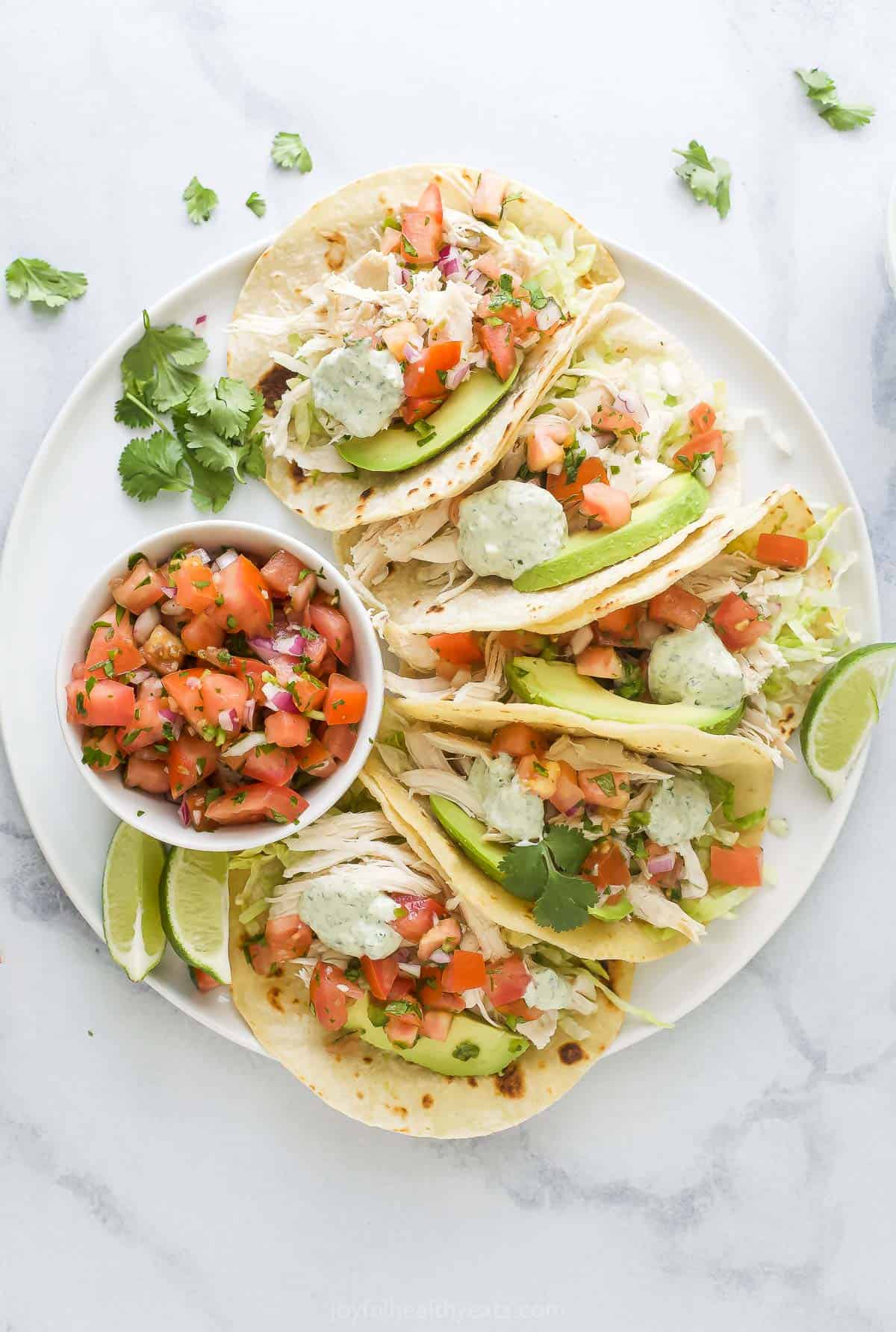 Assembled chicken tacos with a bowl of the onion-pepper mixture on the side. 