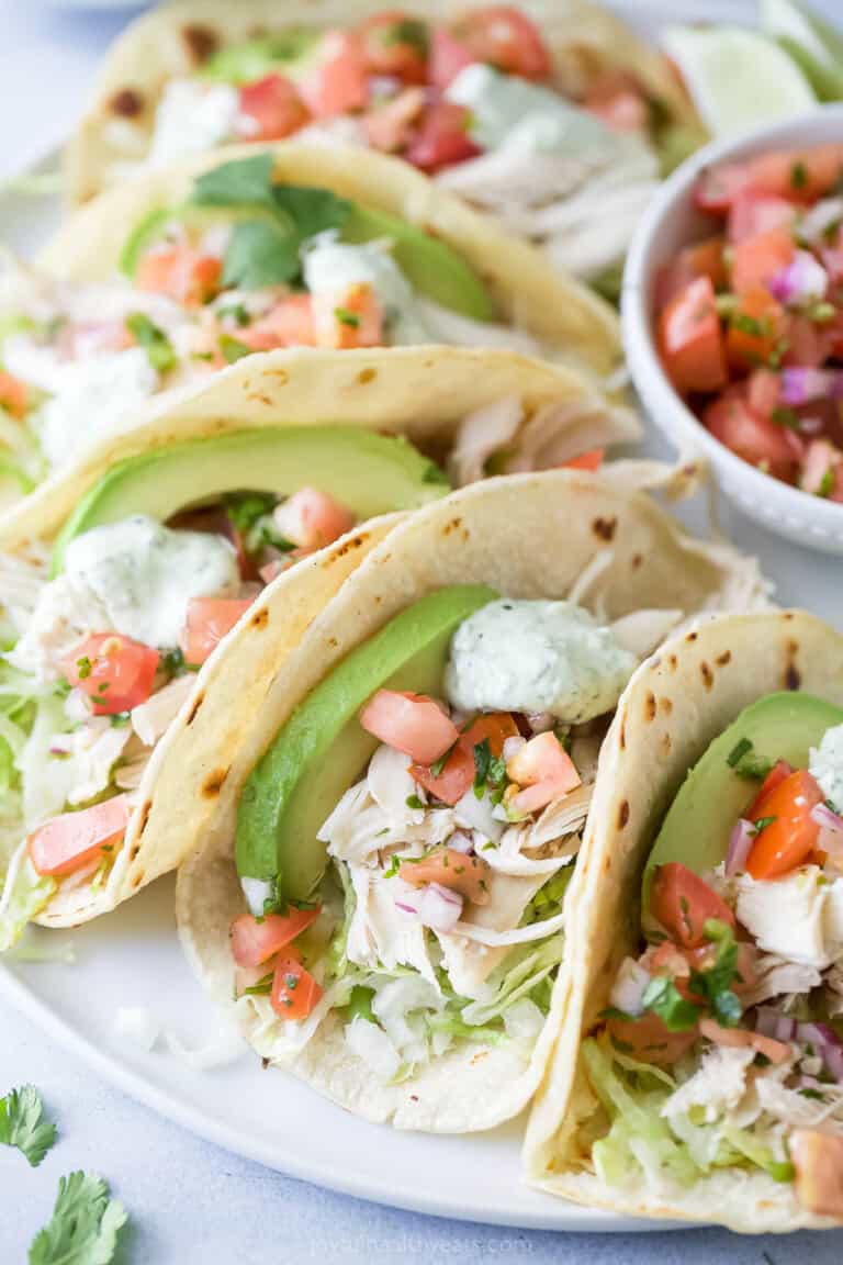 Close-up of tacos with creamy avocado, onion-pepper mixture, cilantro crema, shredded chicken, and lime juice.