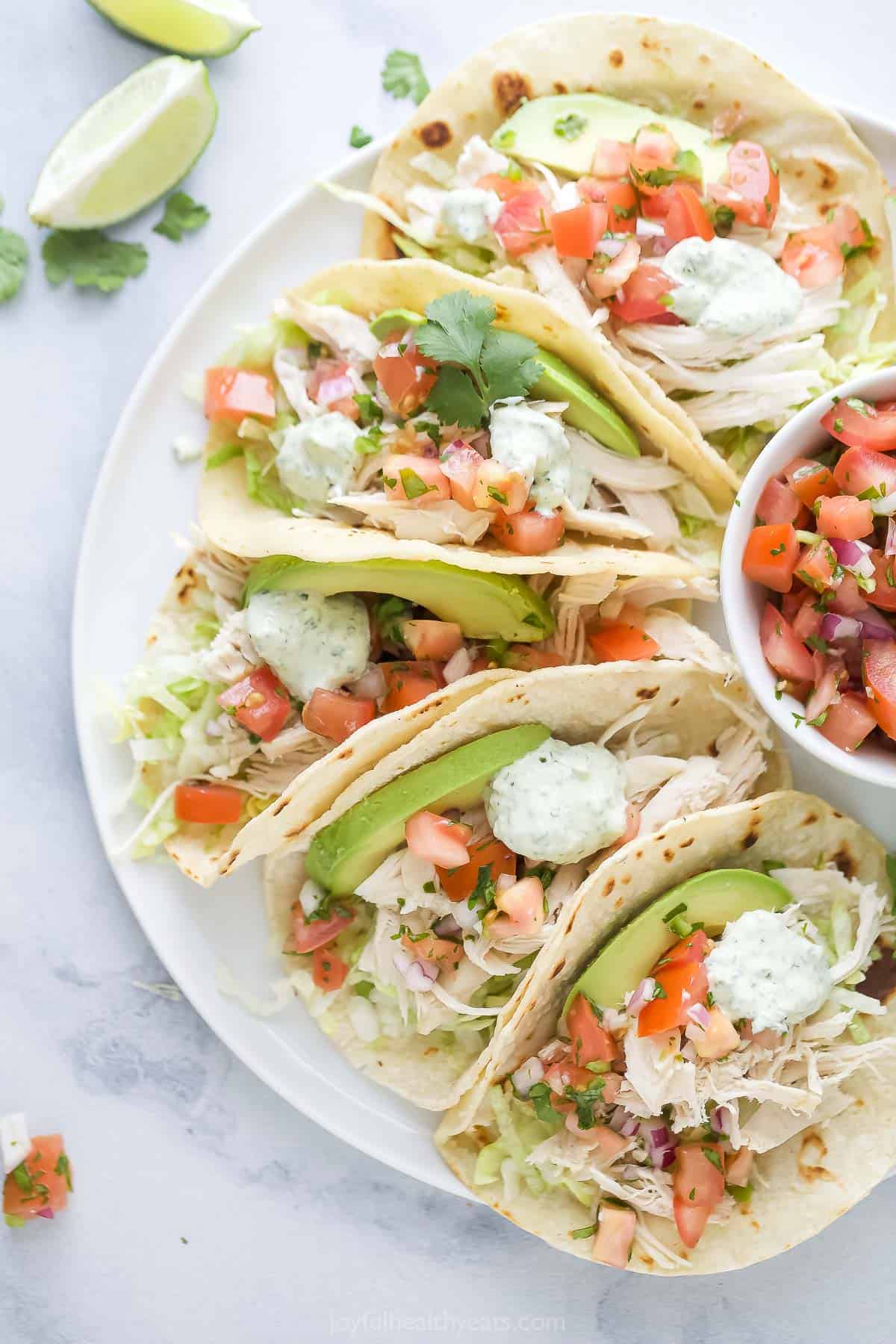 Angled photo of a plate with several shredded chicken tacos with fresh veggie toppings. 