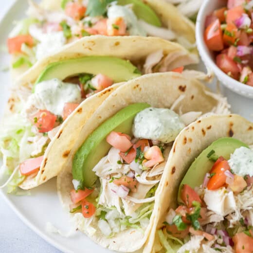 Rotisserie chicken tacos in warm corn tortillas, with avocado, cilantro-lime crema, and other toppings.