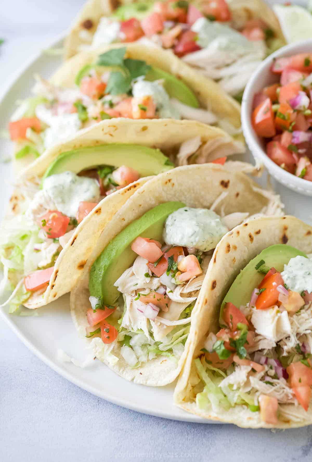 Rotisserie chicken tacos in warm corn tortillas, with avocado, cilantro-lime crema, and other toppings.