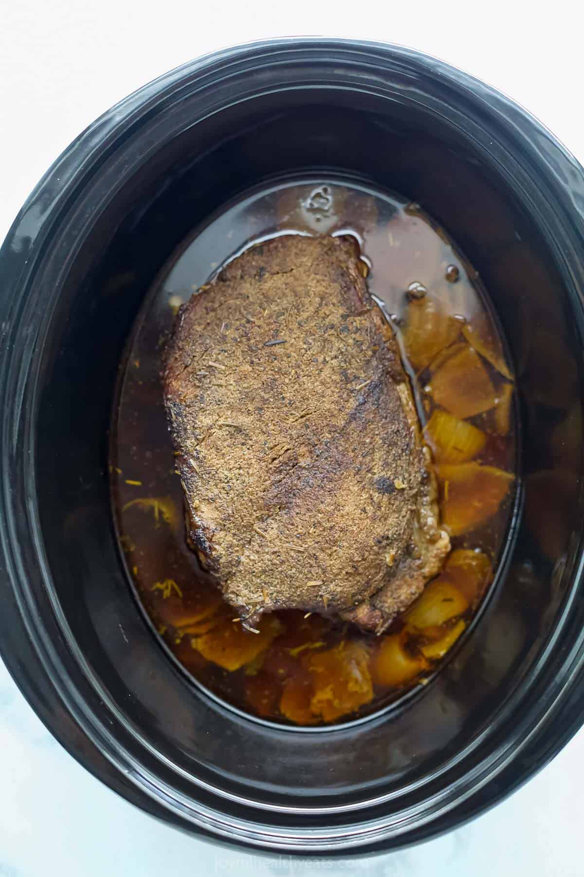 Slow cooked beef in the crockpot with onions, broth, and cooking juices.