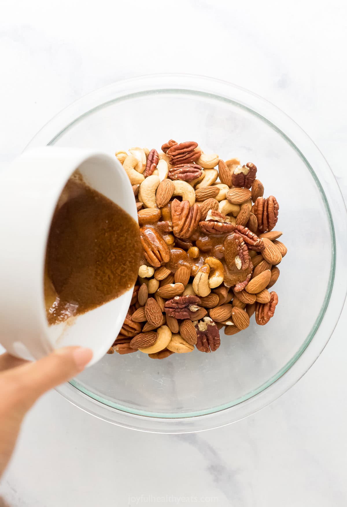 Adding the spiced maple syrup to the bowl of mixed nuts.