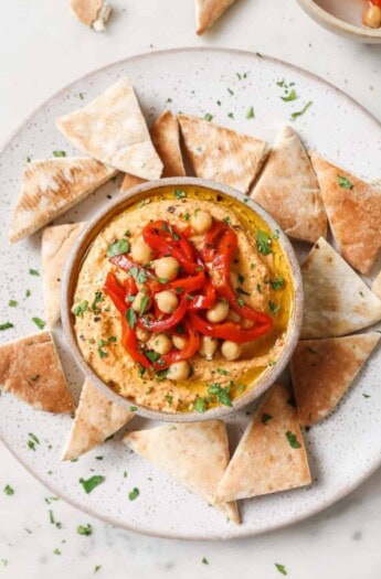 Creamy roasted red pepper hummus with crispy pita chips on the side.