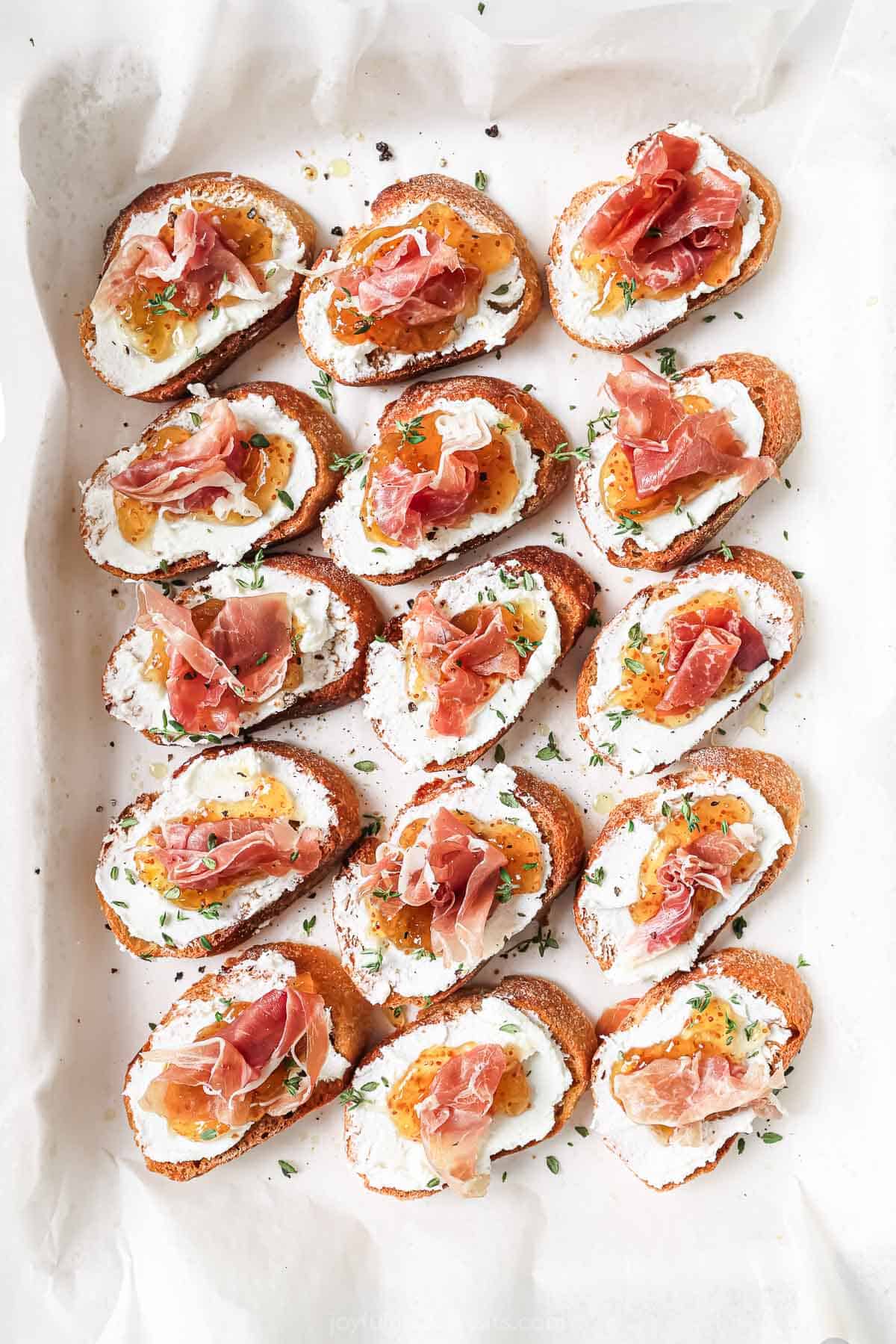 Overhead photo of Italian-inspired appetizer with toasted bread, goat cheese, jam and prosciutto. 