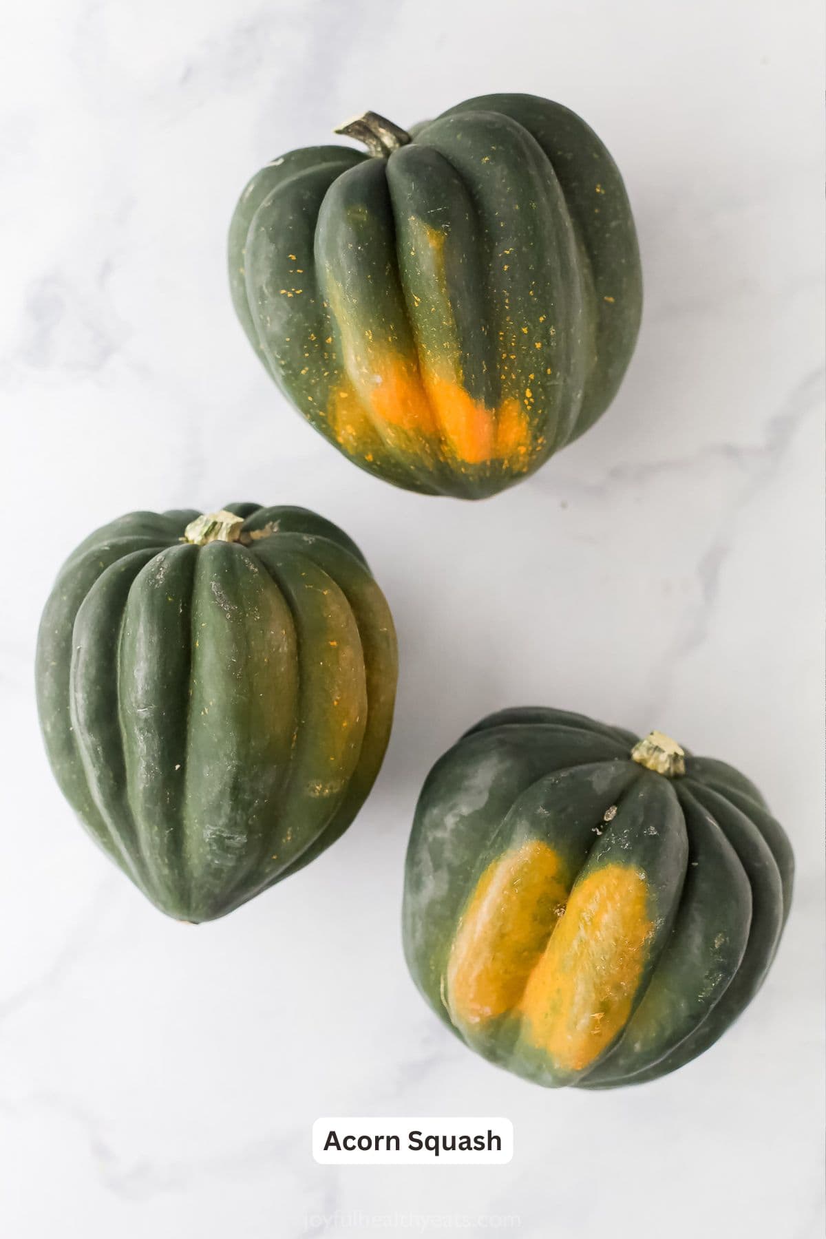 Whole acorn squashes on a marble countertop.