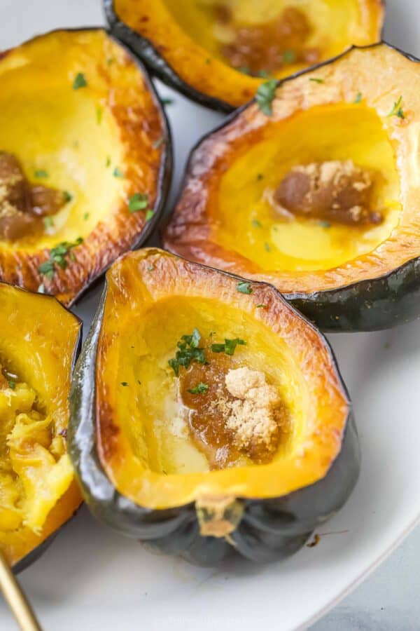 Freshly-roasted acorn squashes on a serving plate with melted butter and brown sugar.