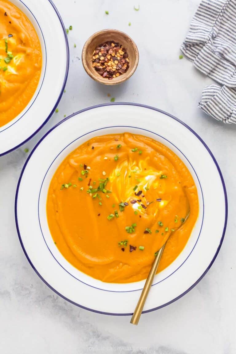 A bowl of homemade carrot ginger soup garnished with yogurt, chives, and red pepper flakes.