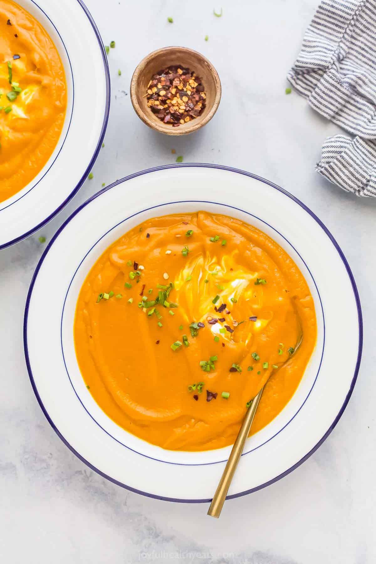 A bowl of homemade carrot ginger soup garnished with yogurt, chives, and red pepper flakes. 