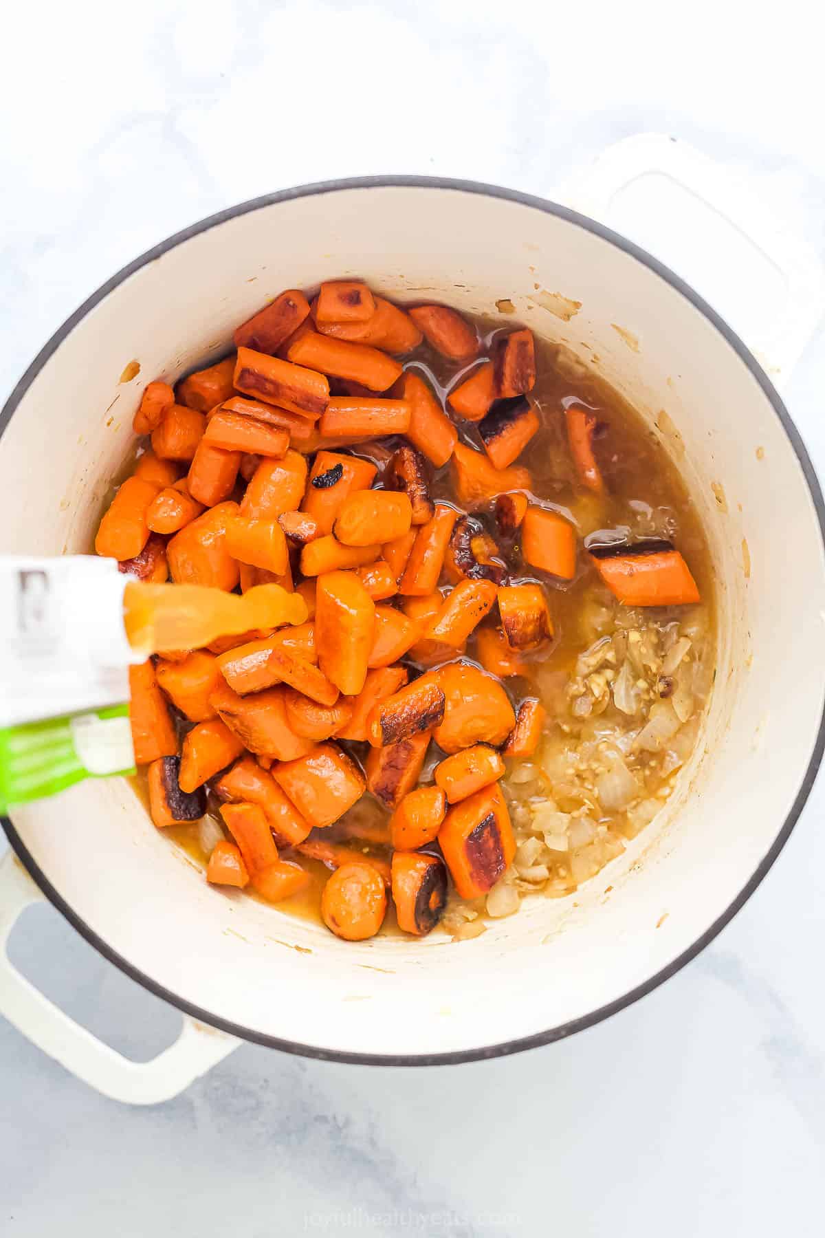 Pouring the veggie stock into the Dutch oven with carrots and onions. 