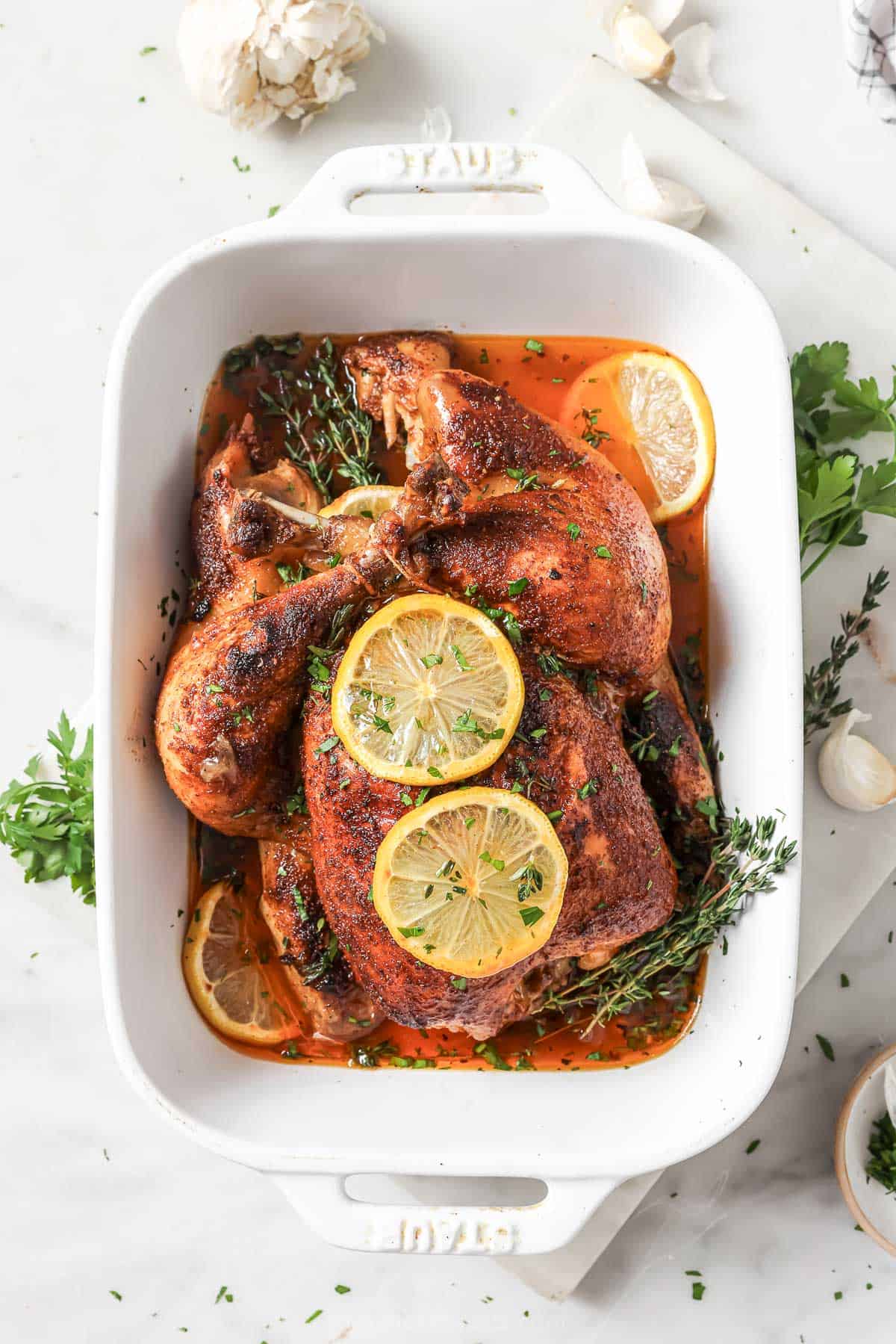 A whole crockpot chicken on a baking dish after broiling, with two slices of lemon on top. 