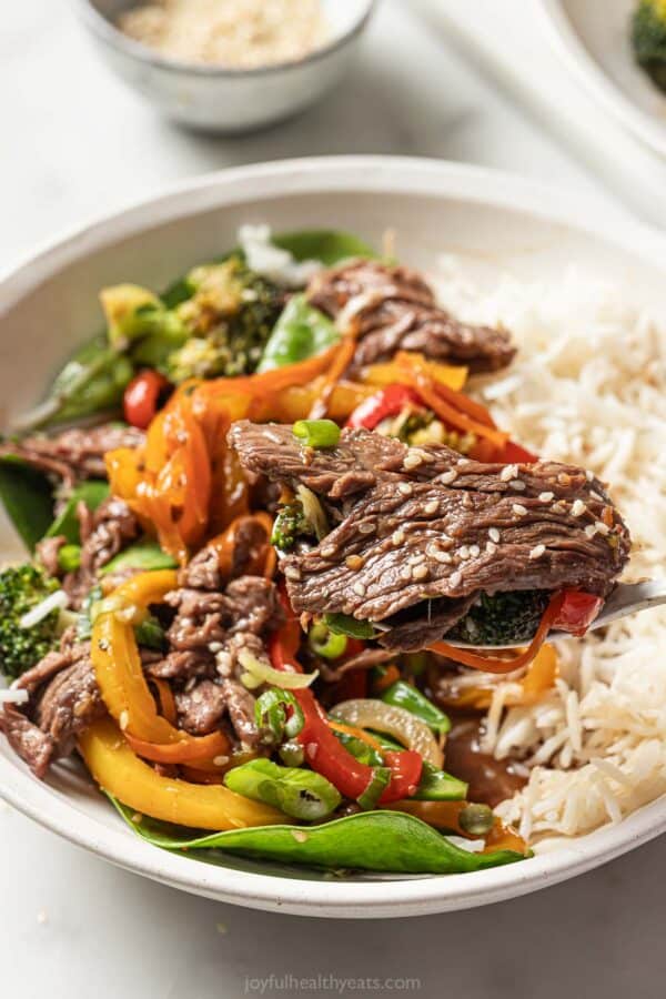 Close-up of a bowl of rice with sweet-and-spicy steak-veggie stir fry on top.