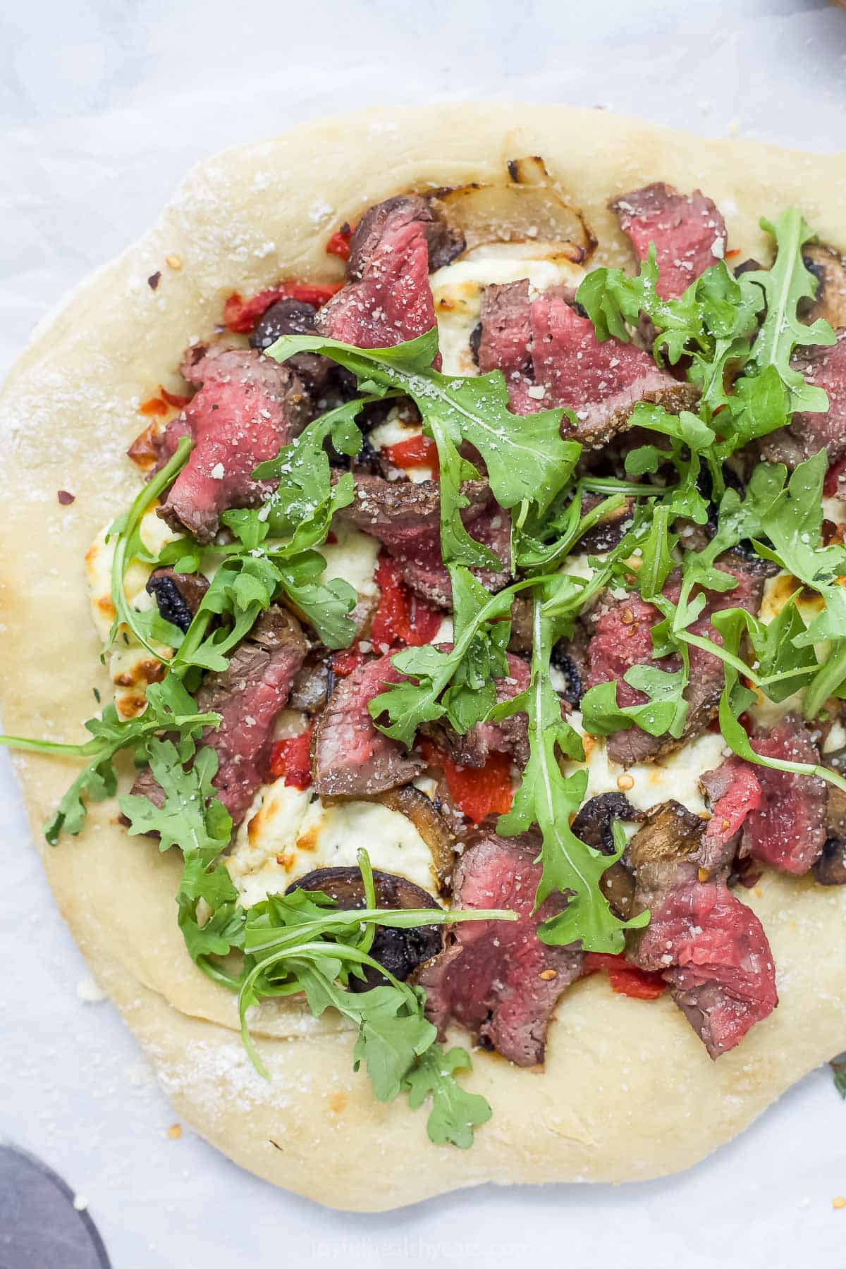 Overhead view of steak pizza with arugula and whipped goat cheese