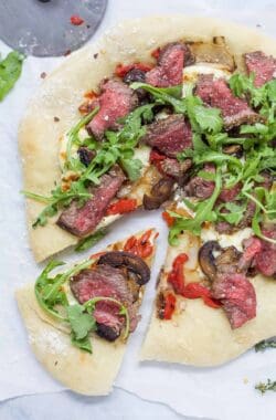 Overhead view of steak pizza with one slice pulled away