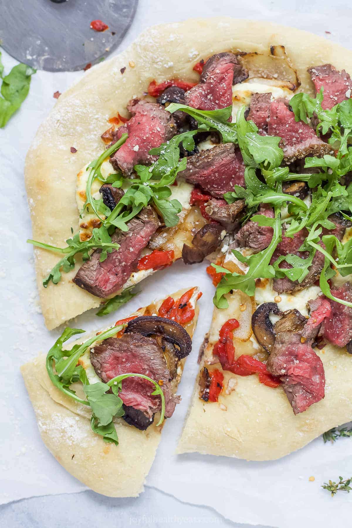 Overhead view of steak pizza with one slice pulled away