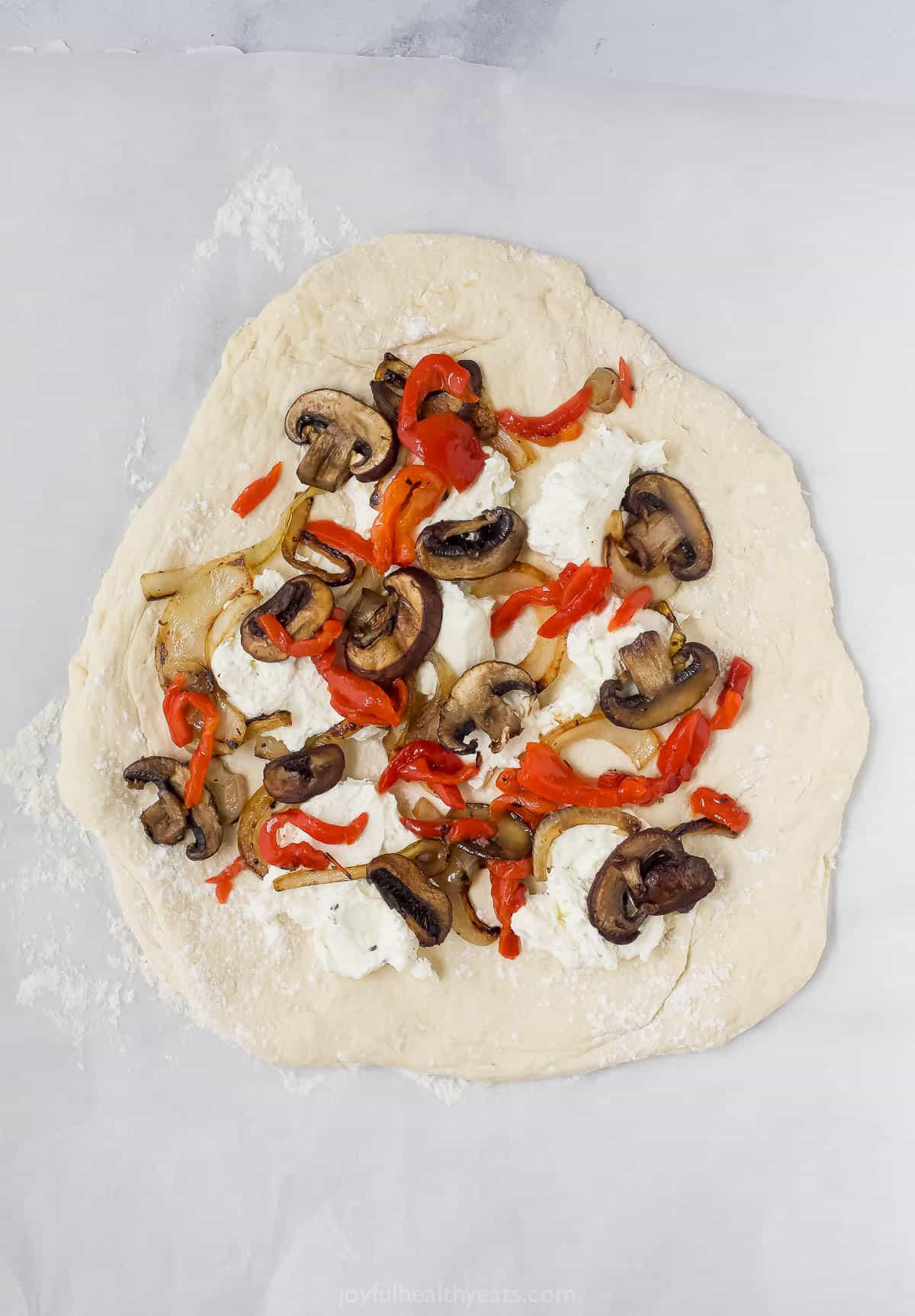 Overhead view of pizza dough topped with whipped goat cheese, onions, mushrooms, and red peppers