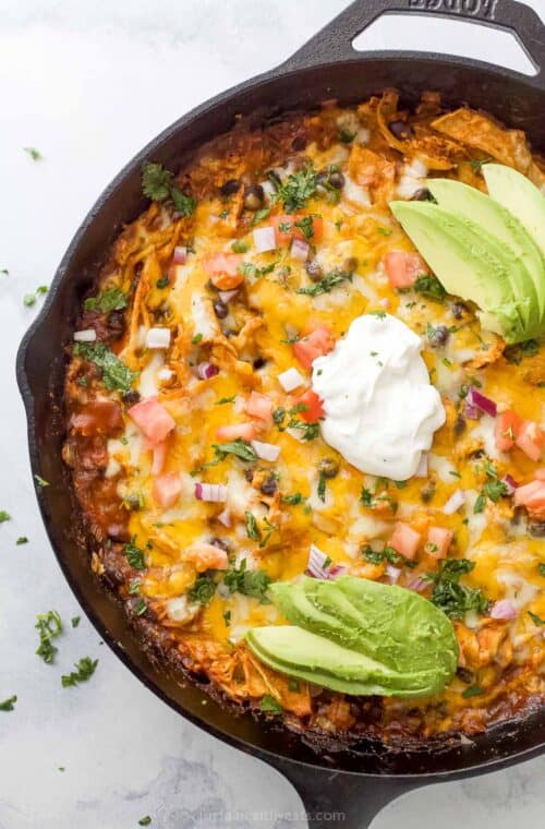 Chicken enchilada casserole with pico de gallo, sour cream, and sliced avocado on top.