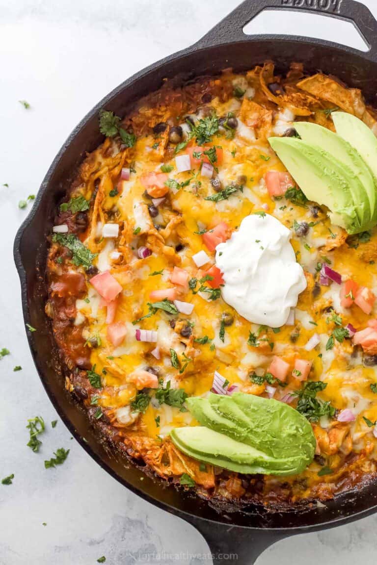 Chicken enchilada casserole with pico de gallo, sour cream, and sliced avocado on top.