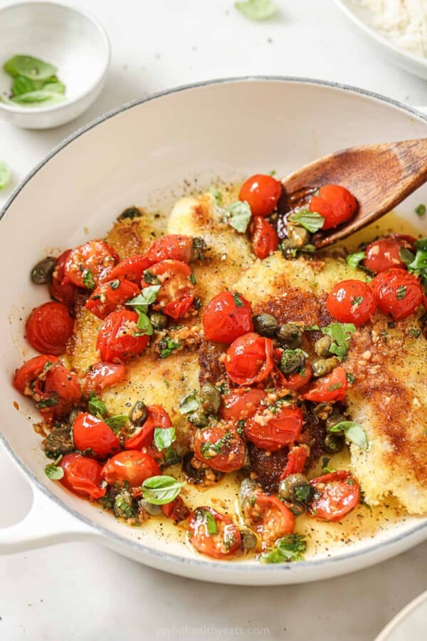 Close-up of flaky panko crusted tilapia with tomato-basil sauce and tender capers.