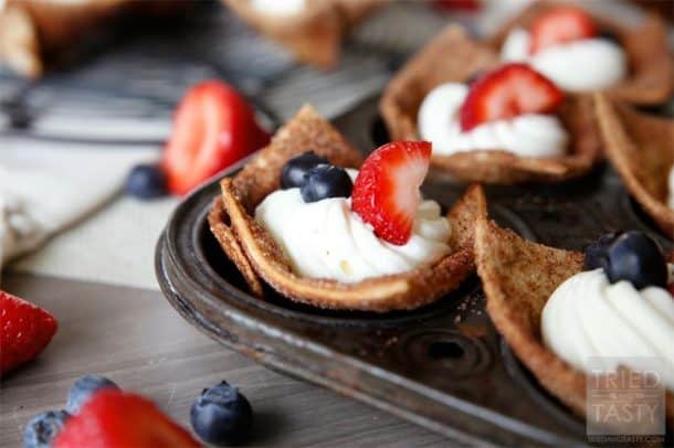 Un moule à muffins avec des coupes de tortilla rouges, blanc et bleu garnis de crème fouettée et de baies fraîches