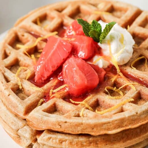 Stack of oatmeal waffles on plate with strawberry compote and whipped cream