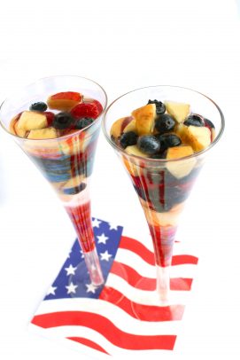 Tall cocktail glasses two filled with fruit and white sangria on an American flag napkin