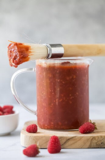 Small pitcher of raspberry chipotle BBQ sauce with a brush on top.