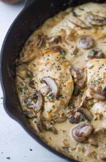 Close-up of juicy chicken with creamy coconut-mushroom sauce and sautéed onions in the skillet.