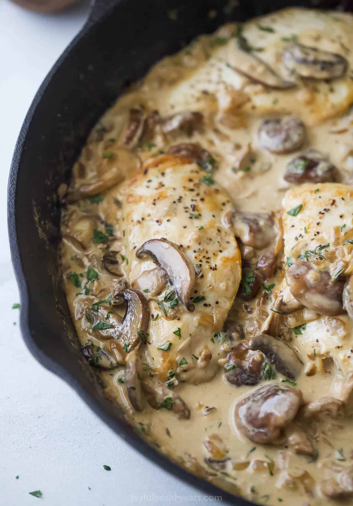 Close-up of juicy chicken with creamy coconut-mushroom sauce and sautéed onions in the skillet.