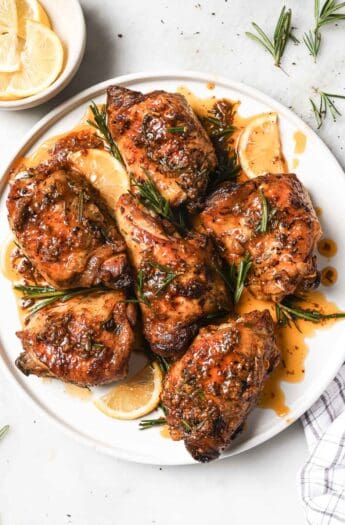 Juicy lemon rosemary chicken with cooking juices on a serving plate.