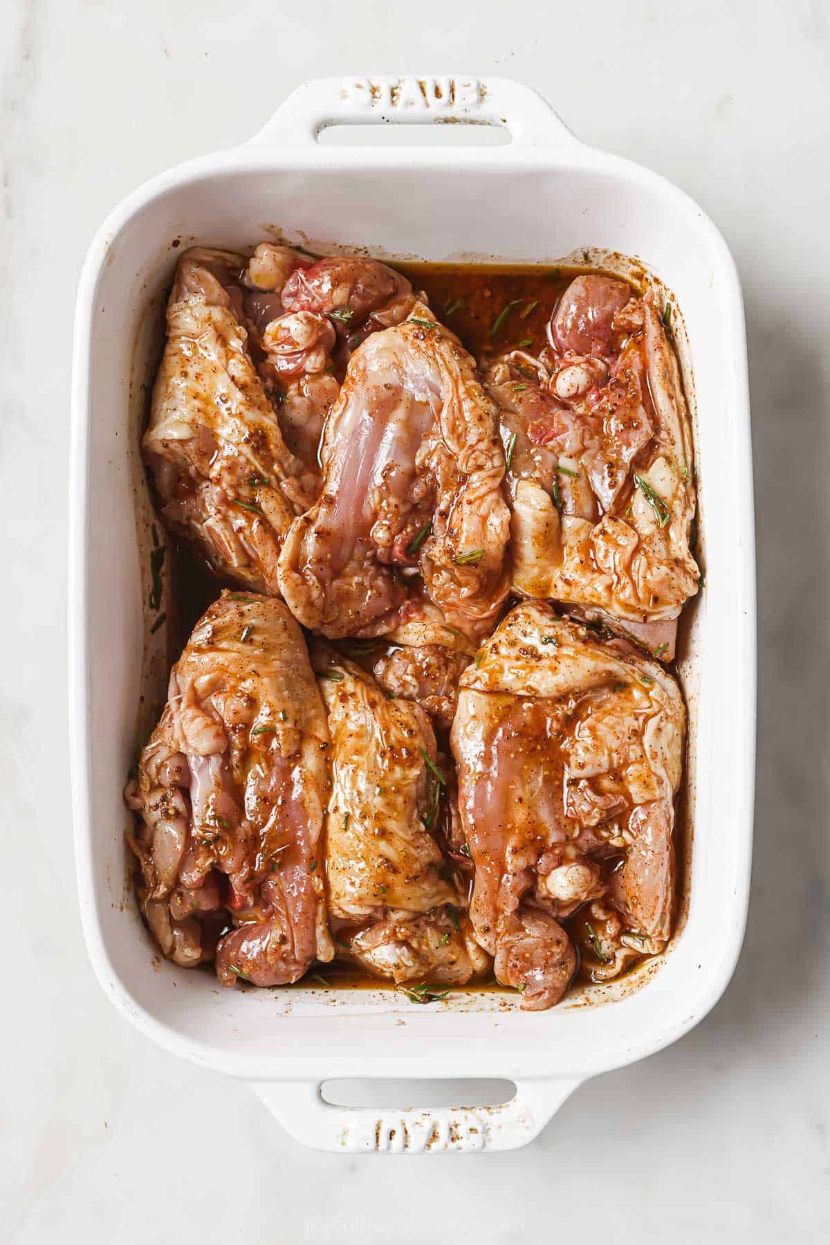 Raw, seasoned chicken thighs in the baking dish with the skin-side facing down.