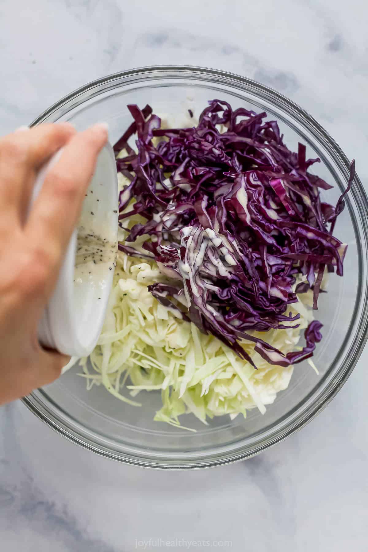 Pouring dressing into bowl of red and green cabbage