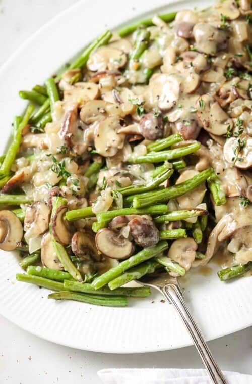 Serving plate of roasted green beans and mushrooms with coconut-thyme sauce.