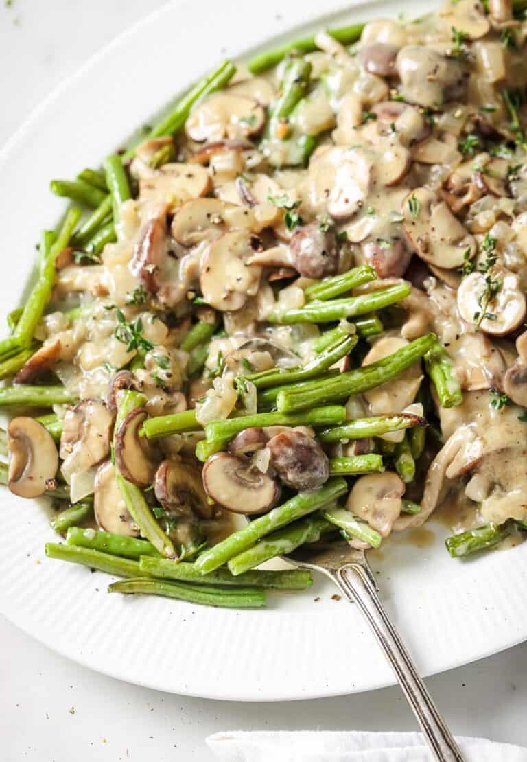 Serving plate of roasted green beans and mushrooms with coconut-thyme sauce.